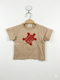 Front view of an authentic Celine baby tan t-shirt featuring a red turtle graphic, hanging on a wooden-style hanger against a Tiny Thrift Store branded background.