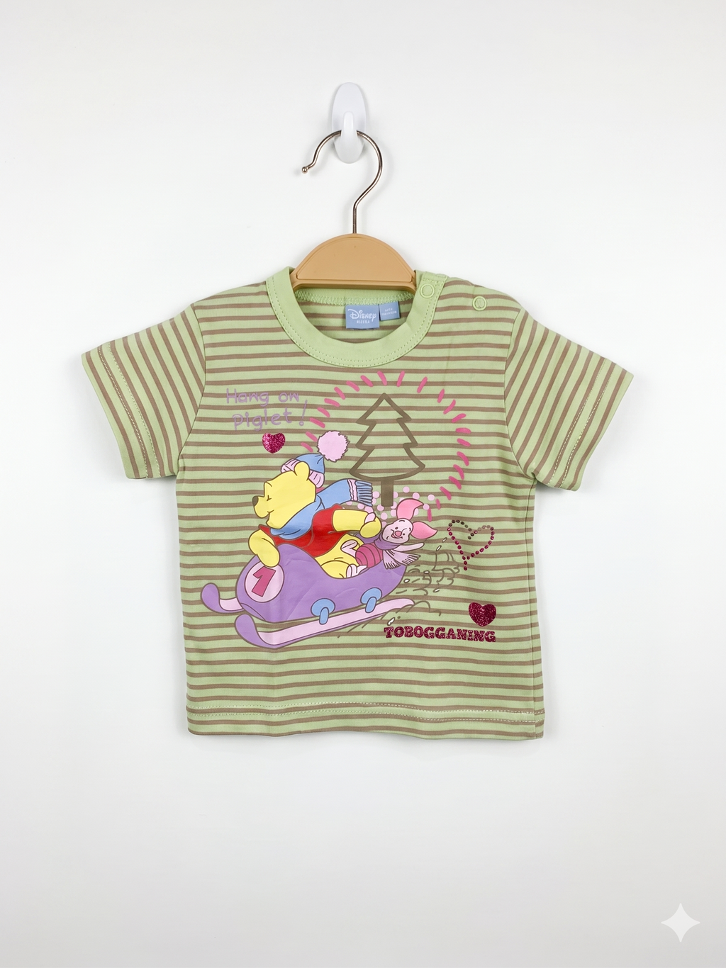 Front and back view of a light green striped Disney Baby t-shirt featuring Winnie the Pooh and Piglet on a sled. The shirt is displayed on a hanger against a Tiny Thrift Store background.