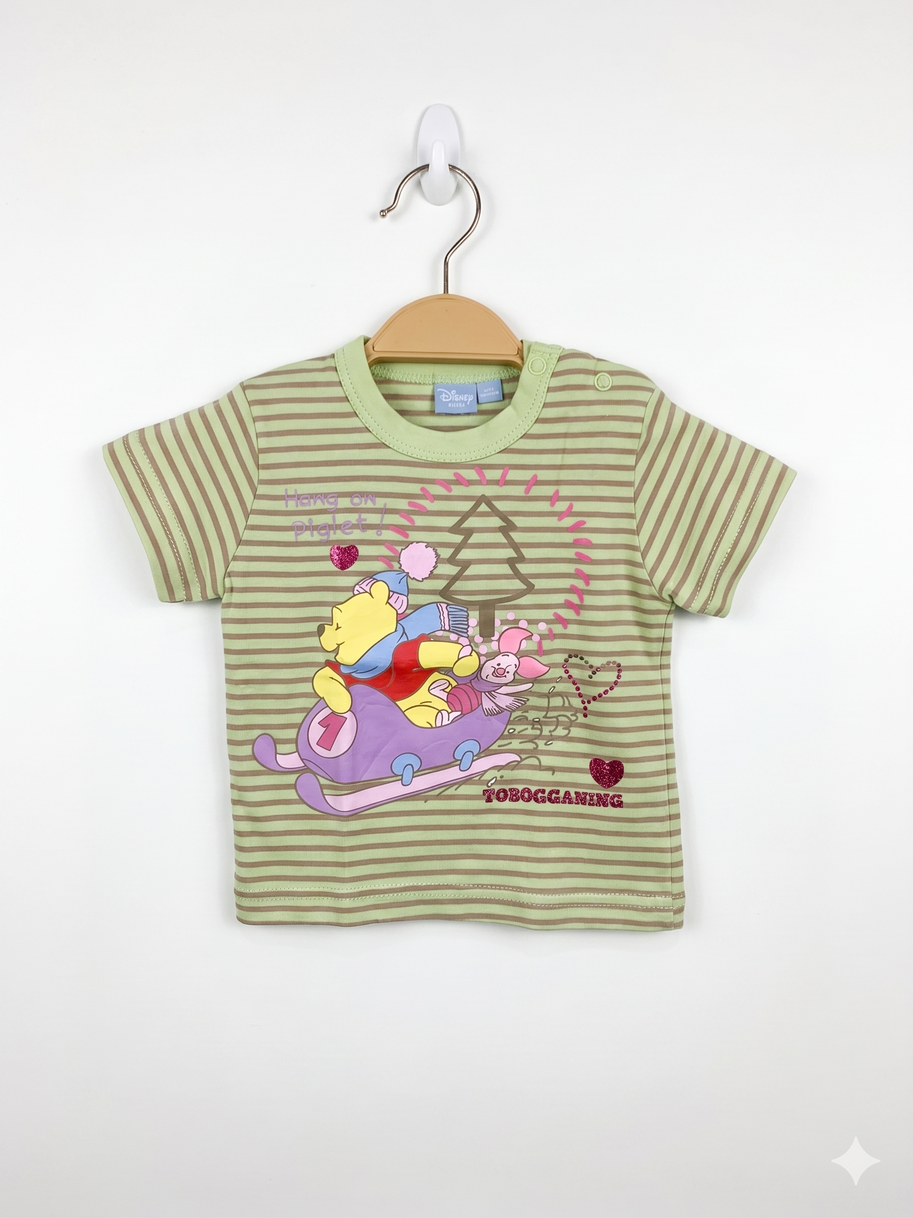 Front and back view of a light green striped Disney Baby t-shirt featuring Winnie the Pooh and Piglet on a sled. The shirt is displayed on a hanger against a Tiny Thrift Store background.