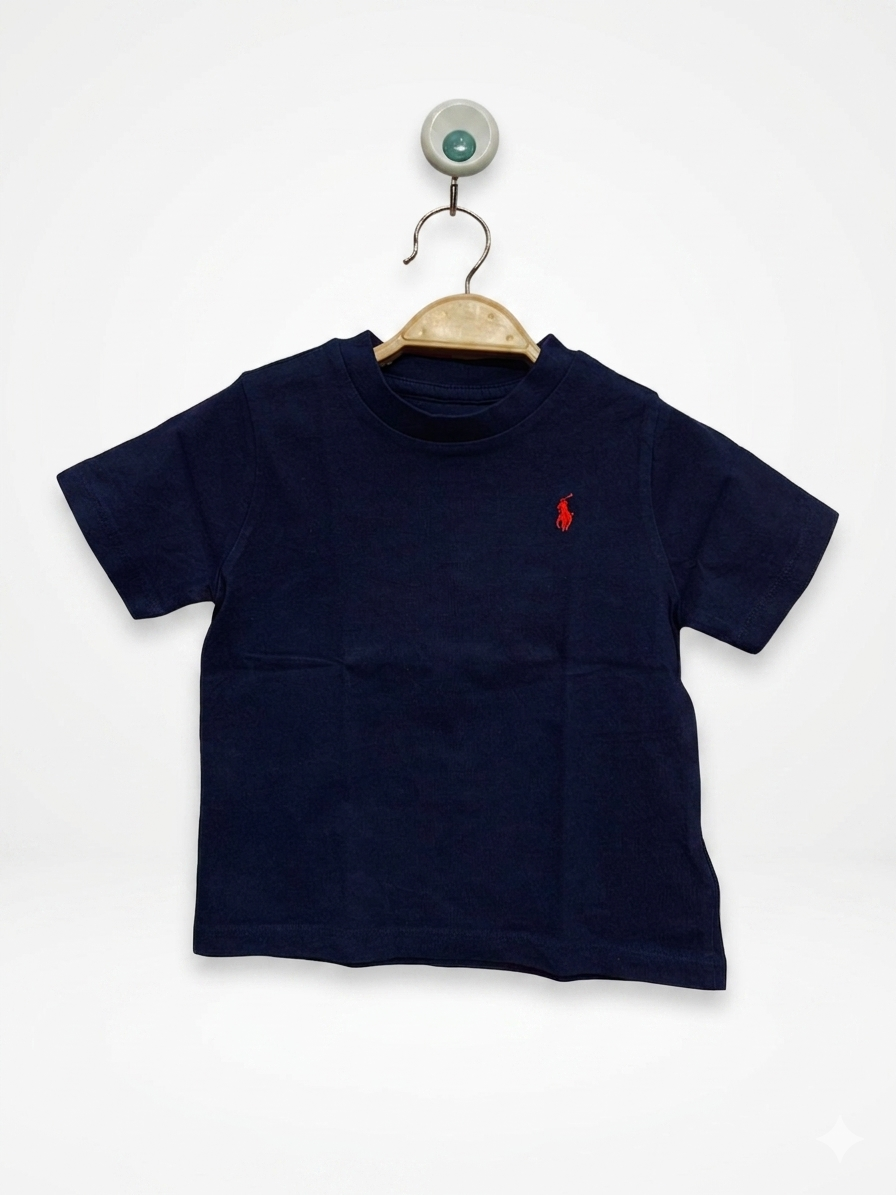 Front and back view of a Ralph Lauren baby boys' navy blue short-sleeved t-shirt. The front features a small, signature red embroidered polo player logo on the left chest. The shirt is displayed on a wooden hanger against a colorful Tiny Thrift Store backdrop. A close-up shows the authentic Ralph Lauren neck label indicating size 18M.