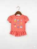 A vibrant coral short-sleeve one-piece swimsuit for toddler girls by Cat & Jack, featuring colorful summer icons like pineapples and sailboats with a peplum ruffle, hanging on a white hanger at Tiny Thrift Store.