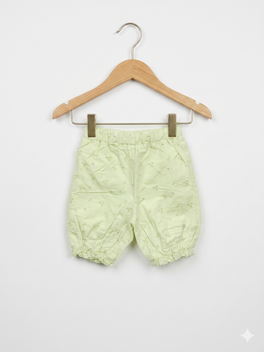Newborn baby girl bloomers in pale lime green with white floral eyelet embroidery, featuring elastic waist and leg cuffs, displayed on a pink hanger at Tiny Thrift Store.
