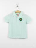 Front and back view of a children's pastel mint green short-sleeved polo shirt hanging on a wooden hanger. The shirt features a two-button collar and a colorful embroidered circular crest on the left chest with the word "STATE" and a shield. The fabric has a classic textured pique weave.