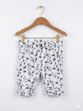 A pair of white girls' capri pants with a navy blue floral print hanging on a white hanger against a colorful Tiny Thrift Store backdrop. The pants feature ruffle hems and small bows at the waist.