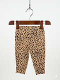 Baby girls leopard print leggings by Carter's, size 9 months, featuring a realistic cheetah pattern on a tan background, hung on a pink hanger against the Tiny Thrift Store backdrop.