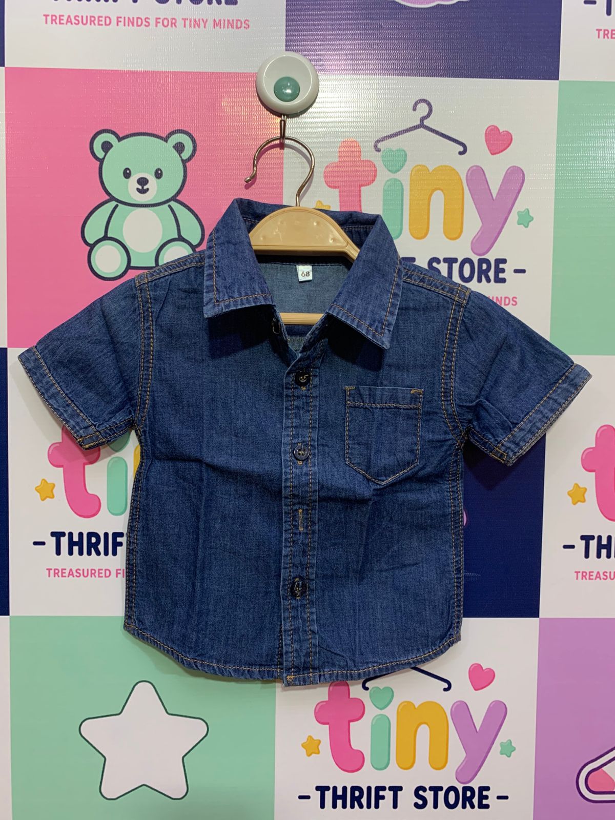 Front and back view of a baby boy's short-sleeve blue denim shirt. It has a collar, buttons down the front, and a small pocket on the left. Close-up shows a white size tag with the number "68".