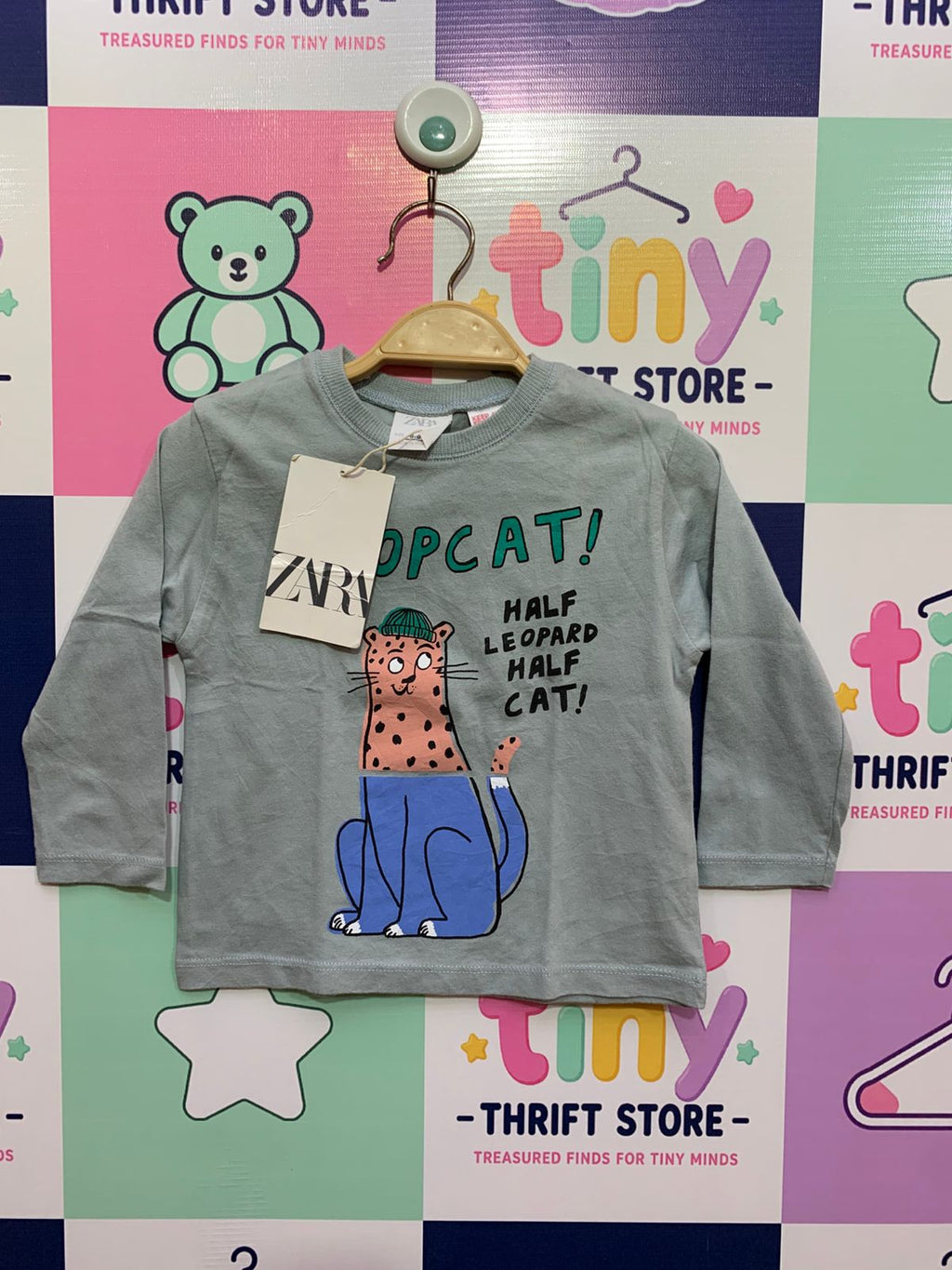 Front and back view of a light sage green baby boy's long-sleeve t-shirt with a full graphic of a stylized leopard. A close-up view of the internal tag shows the "ZARA" logo, "Size 6-9 Months," and "MADE IN PORTUGAL" with a white paper price tag attached.