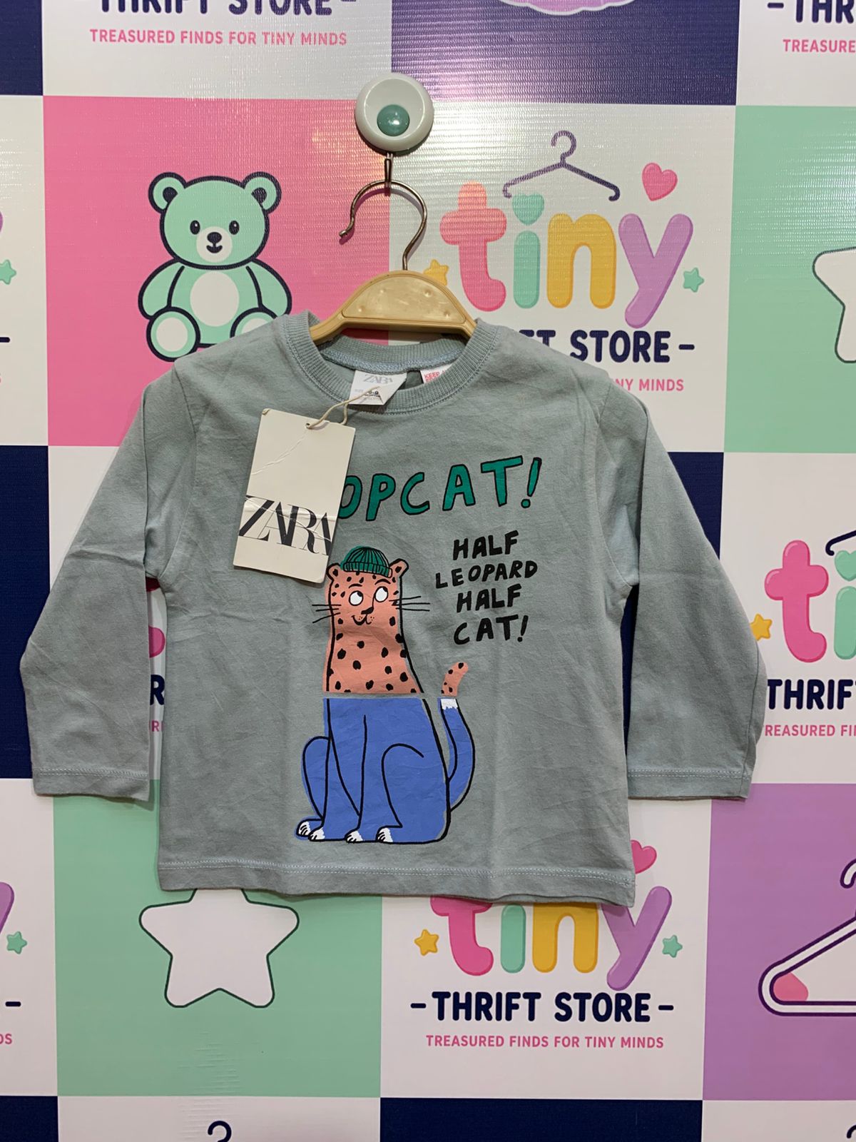 Front and back view of a light sage green baby boy's long-sleeve t-shirt with a full graphic of a stylized leopard. A close-up view of the internal tag shows the "ZARA" logo, "Size 6-9 Months," and "MADE IN PORTUGAL" with a white paper price tag attached.