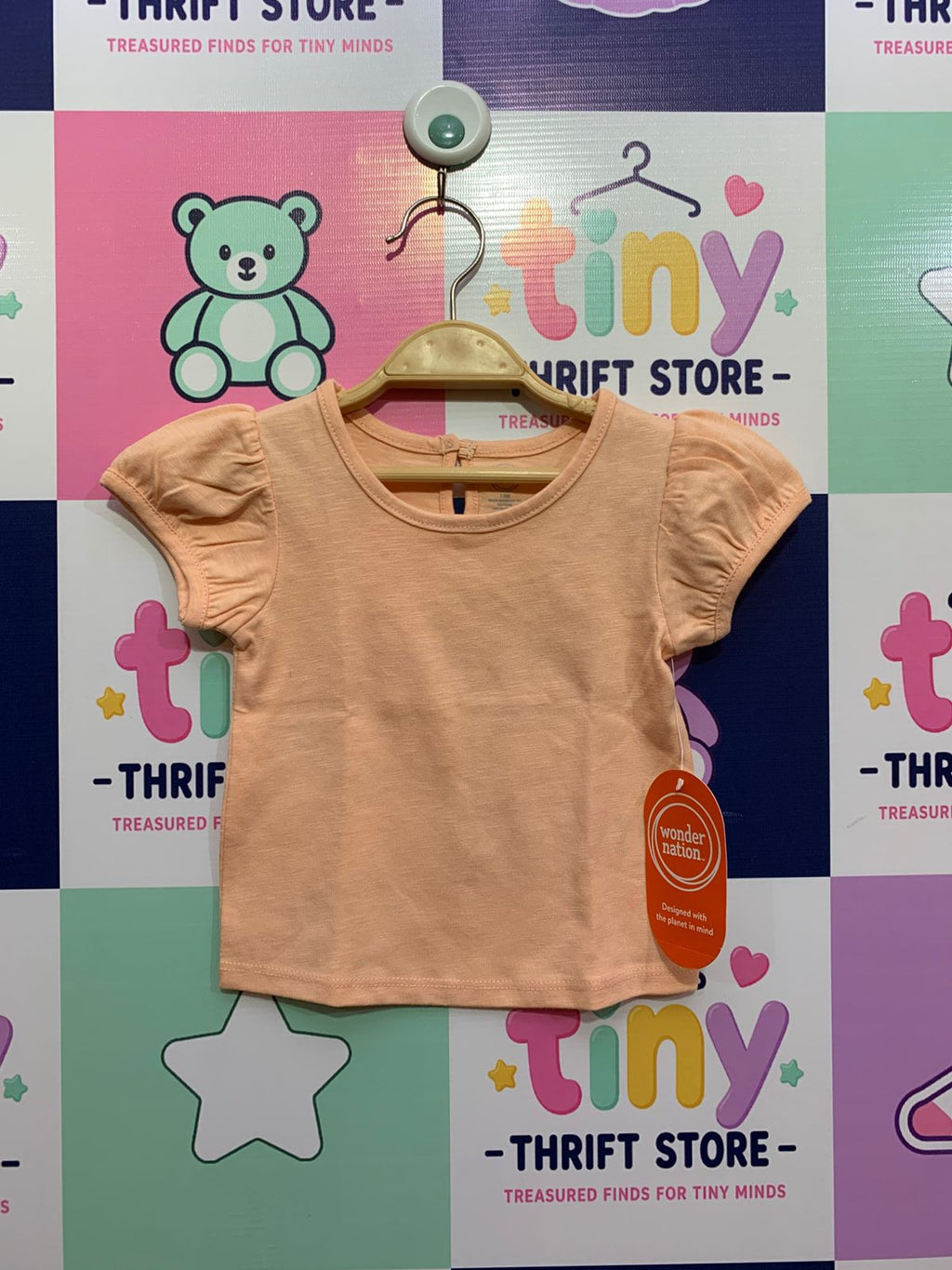 Front view of a peach-colored Wonder Nation baby girl t-shirt with puff sleeves and original price tag, displayed against a colorful Tiny Thrift Store backdrop.
