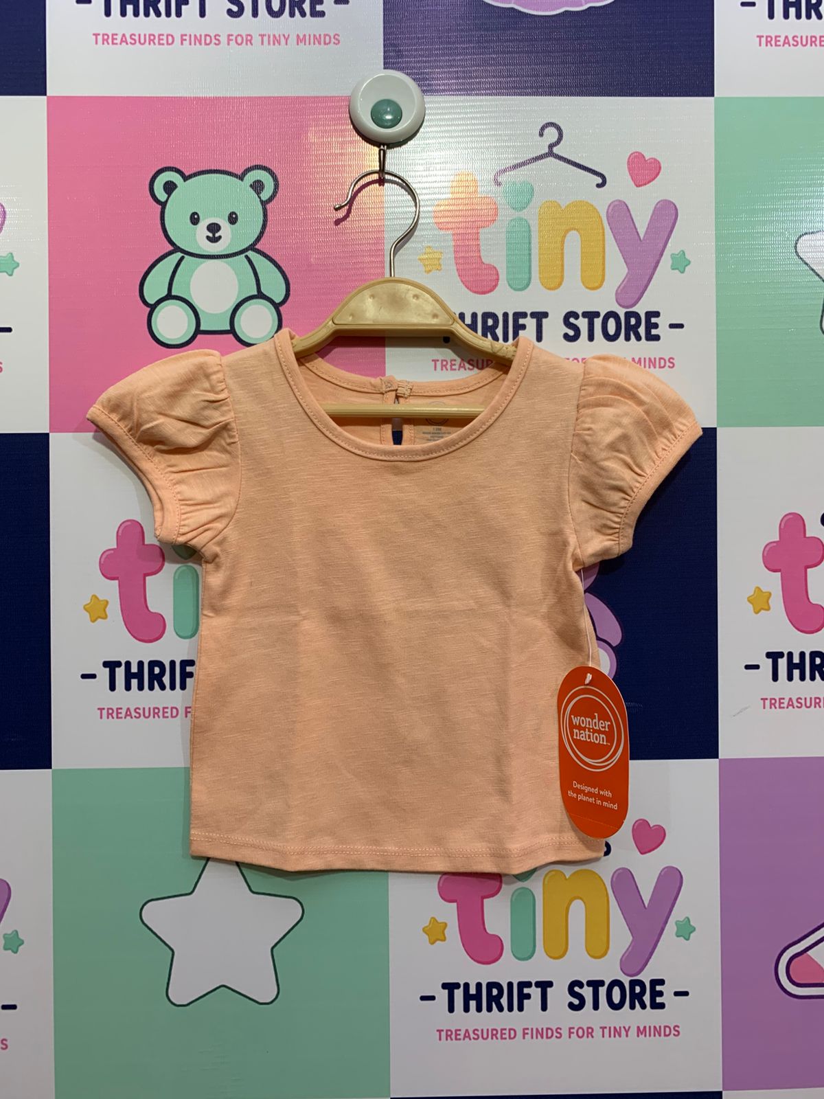 Front view of a peach-colored Wonder Nation baby girl t-shirt with puff sleeves and original price tag, displayed against a colorful Tiny Thrift Store backdrop.