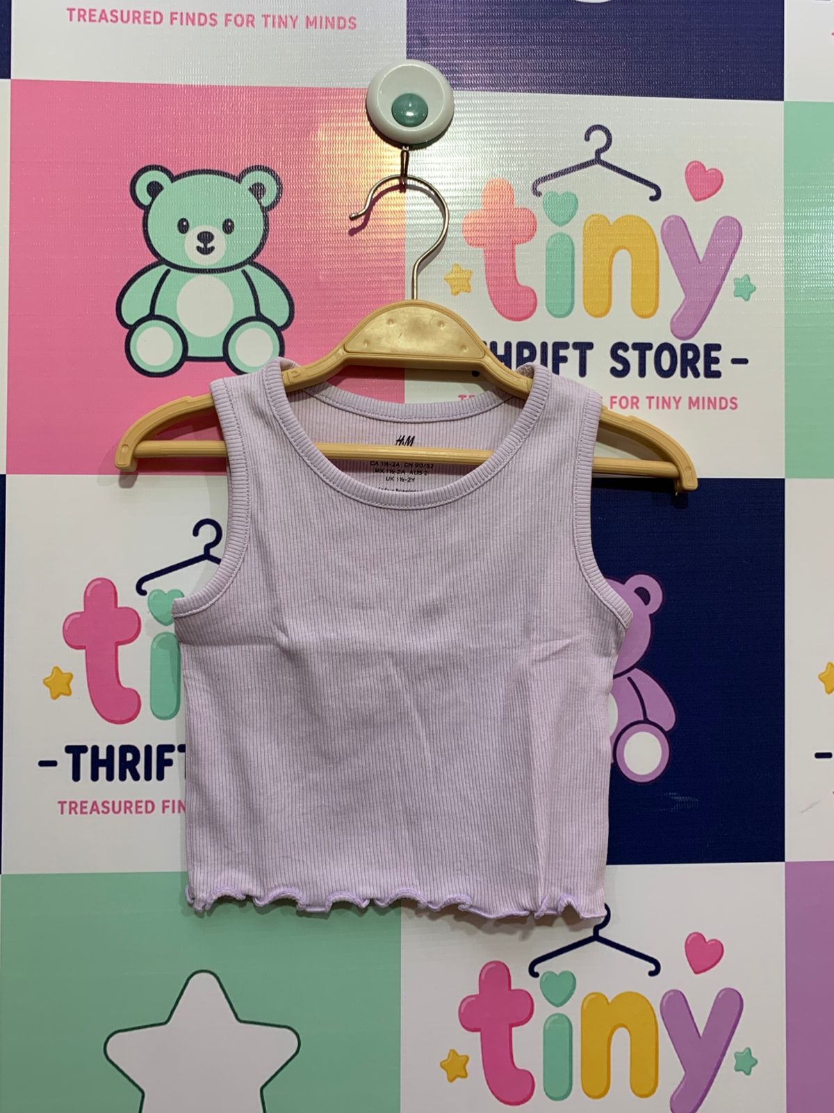 H&M brand toddler girl lilac purple ribbed tank top with lettuce-edge hem on a wooden hanger showing size US 2T EUR 92 label for professional e-commerce store listing.