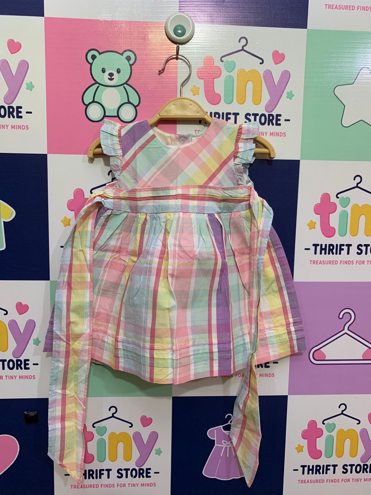 Front view of Chaps baby girls multi-color pastel plaid dress with ruffle sleeves and tie-back belt.