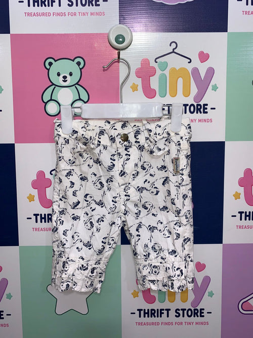 A pair of white girls' capri pants with a navy blue floral print hanging on a white hanger against a colorful Tiny Thrift Store backdrop. The pants feature ruffle hems and small bows at the waist.